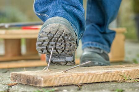 Arbeiter mit Sicherheitsschuhen tritt in einen Nagel